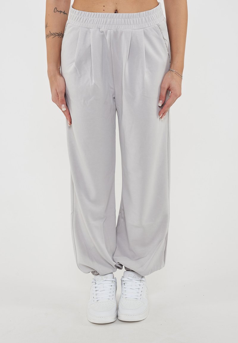 Pantaloni in tessuto grigio chiaro con vestibilità morbida, design plissettato, cintura elastica e tasche laterali, abbinati a sneaker bianche.