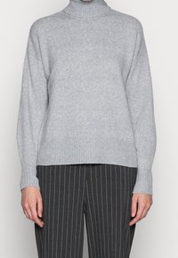 Helles graues Rollkragensweatshirt aus weichem Strickstoff, mit geripptem Kragen und Bündchen, im lässigen Schnitt. Kombiniert mit gestreiften Hosen.