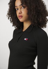 Camiseta polo negra de canalé con tapeta de botones, que presenta un pequeño logo multicolor de 'Tommy Jeans' en el lado izquierdo del pecho.