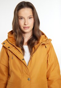 Giacca impermeabile gialla con cappuccio, chiusura frontale a bottoni e zip, e tasche laterali. Caratterizzata da una texture liscia e hardware resistente.