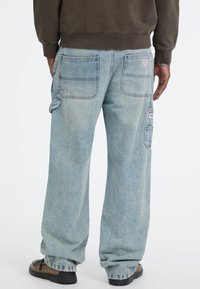 Pantaloni cargo in denim azzurro chiaro con vestibilità rilassata, due tasche posteriori, tasca laterale e sfumature leggere. Indossati con una felpa scura.