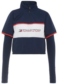 Marineblau und weiße kurze Jacke mit einem Halb-Reißverschlusskragen, kurzen Ärmeln und roten Akzenten. Enthält ein Logo auf der Vorderseite und einen elastischen Bund.
