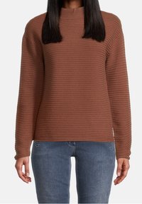 Brun ribbad pullovertröja med hög hals och långa ärmar, i kombination med blå jeans med dekorativa detaljer på fickorna.