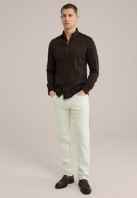 Temno rjava srajca z dolgimi rokavi in gumbi, v kombinaciji z off-white hlačami in črnimi loafers. Gladka tekstura, standardna zasnova ovratnika.