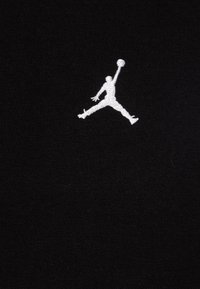 Un tessuto nero presenta un logo Jumpman bianco, raffigurato in volo con un pallone da basket. Texture liscia, design minimalista.