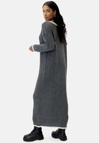 Vestido gris de punto acanalado con mangas largas y un cuello en contraste color crema, que llega hasta la mitad de la pantorrilla, combinado con botas negras de plataforma.