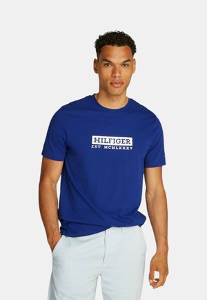 T-shirt in cotone blu con maniche corte. La parte anteriore presenta la scritta bianca "HILFIGER EST. MCMLXXXV". Vestibilità regolare con scollo a giro.