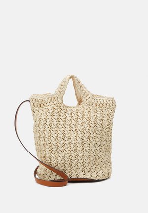 Sac cabas beige tissé avec des poignées courtes et une longue bandoulière marron réglable sur un fond uni.