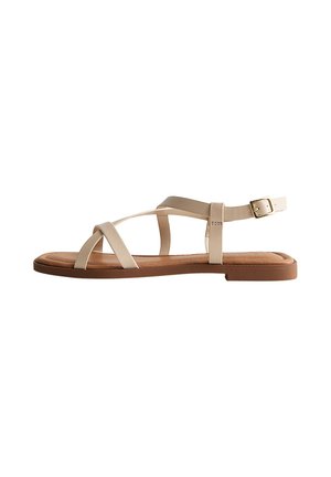 Platte sandalen in beige met gekruiste bandjes, een enkelbuckle en een gevoerde zool, zijaanzicht op een witte achtergrond.