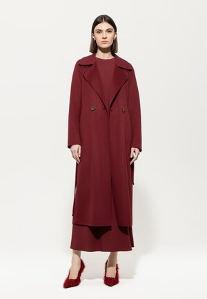 Burgundy wool blend coat with a notched collar, double-breasted button closure, and two side slits. Paired with matching dress and textured red shoes.