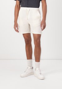 Shorts légers beiges en tissu texturé. Équipés d'une taille élastique avec cordon de serrage, de poches latérales et d'une coupe décontractée.