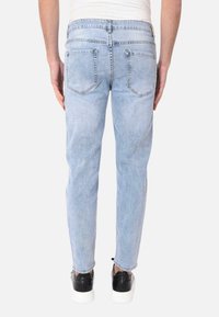 Jeans azzurri chiari con vestibilità dritta, dotati di tasche posteriori e un leggero effetto sbiadito. Indossati con scarpe nere e una camicia bianca.