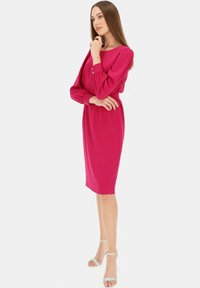 Fuksjowa sukienka z długimi rękawami, okrągłym dekoltem i guzikowymi akcentami na mankietach. Gładki, lekki materiał z dopasowanym krojem kończącym się na kolanach.