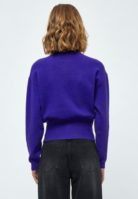 Maglione a maglia viola con scollo rotondo e spalle basse, abbinato a jeans in denim neri a vita alta. Tessuto strutturato, vestibilità casual.
