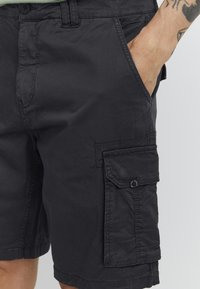 Shorts cargo noirs en tissu léger, dotés de poches latérales, d'une fermeture à bouton à l'avant et de détails de couture visibles.