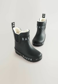Bottines noires imperméables avec la marque blanche "BAKER" et "BY TED BAKER". Doublées de fausse fourrure blanche, avec une semelle en caoutchouc texturé.
