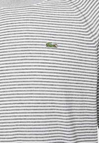 Chemise à rayures horizontales blanches et grises avec un petit logo de crocodile vert brodé sur la poitrine.