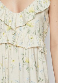Robe en tissu léger avec un imprimé floral jaune et bleu, dotée d'un col volanté et d'une conception à volants. Texture douce et silhouette fluide.