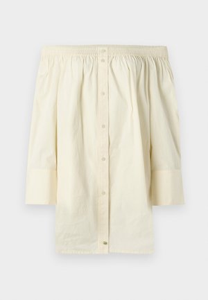 Off-the-shoulder, cream-colored top made of cotton. Features gathered neckline, button-up front, and three-quarter length sleeves.