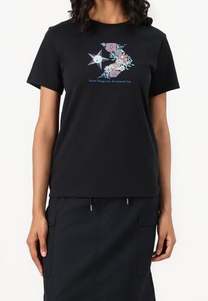 T-shirt en coton noir avec un graphique coloré de fleurs et d'étoiles, avec le texte "De bonnes choses vous entourent" en bleu. Manches courtes.