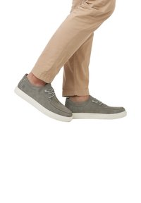 Graue Wildlederschuhe mit weißer Gummisohle, ausgestattet mit grauen Schnürsenkeln und einem schlanken Design. Der Schuh hat sichtbare Nähte und ein Logo.