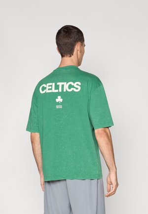 T-shirt vert à manches courtes en tissu doux, arborant un grand texte blanc "CELTICS" et un logo au centre au dos.