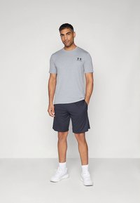 Grå tränings t-shirt med korta ärmar, kombinerad med marinblå shorts och vita sneakers. Har en liten svart logotyp på bröstet.
