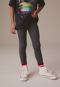 Leggings grises combinados con una camiseta negra con diseños gráficos coloridos, calcetines a rayas rojas y rosas, y zapatillas blancas de caña alta.