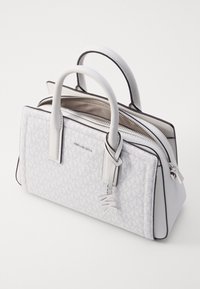 Witte handtas met een gestructureerd patroon, dubbele ritssluiting, glad leren accenten en twee handvatten bovenaan. Beschikt over een metalen charme.