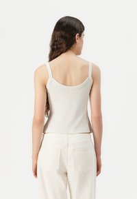 Light beige ribbed tank top with a round back neckline and narrow straps, paired with white wide-leg pants. Casual fit and smooth texture.