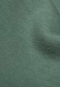 Zielony, żeberkowany materiał o miękkiej teksturze, z delikatnym wzorem plecionki, który pokazuje subtelne różnice w kolorze i głębi.