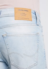 Jeans in denim blu chiaro con etichetta in pelle riportante "JACK & JONES" e un design minimalista, inclusi punti di cucitura discreti sui taschini posteriori.