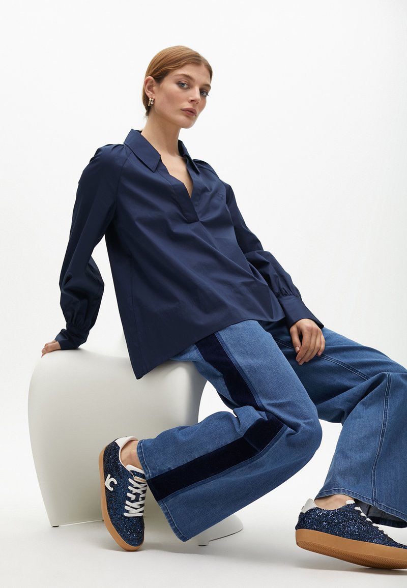 Námorně modrá košile s límečkem a volným střihem, spárovaná s džínami širokého střihu se námořnickým pruhem a modrými třpytivými teniskami.