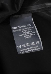 Schwarzes Stoffetikett mit Pflegehinweisen für das Produkt von Swedemount, das mehrsprachigen Text enthält, der Material- und Wartungsdetails angibt.