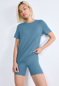 Jasnoniebieska koszulka z krótkim rękawem w połączeniu z dopasowanymi szortami, obie wykonane z gładkiego, miękkiego materiału. Prosty wzór bez widocznych wzorów.