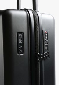 Maleta rígida negra con acabado texturizado, que presenta una cerradura combinada, cierres de cremallera y una placa de logo de Scalpers.