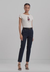 Maglietta bianca a maniche corte con un motivo decorativo, abbinata a pantaloni tailored blu navale e tacchi neri con cinturini. Design semplice e aderente.