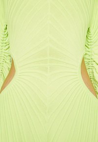 Abito verde lime con texture rigata, caratterizzato da tagli laterali e maniche lunghe arricciate, che mette in risalto una silhouette aderente.