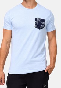 T-shirt in cotone azzurro chiaro con taschino blu navy decorato con un motivo di granchietti bianchi. Maniche corte, colletto rotondo e vestibilità regolare.