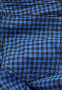 Blue and black checkered fabric with a plaid pattern, featuring a smooth texture and a pocket detail. Ideal for casual wear.