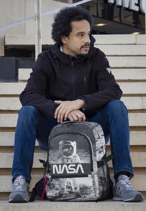 Mochila negra y gris con gráfico de astronauta y logotipo "NASA" en blanco, que cuenta con cremalleras, bolsillos de malla y una tela texturizada.
