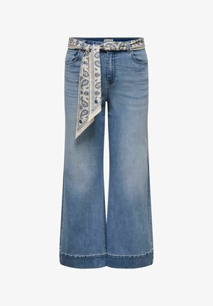 Lyseblå cowboybukser med vide ben og et hvidt bælte med mønster bundet i taljen.