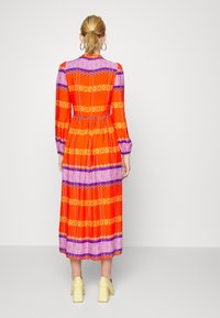 Robe longue orange avec des rayures à motifs violets et jaunes, taille élastique et manches longues. Présente une fermeture en keyhole au dos.
