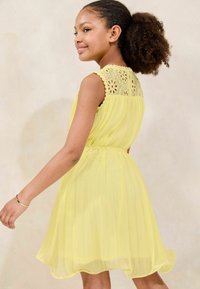 Abito di chiffon giallo con colletto in pizzo, design senza maniche, gonna plissettata e vita arricciata. Texture morbida e silhouette fluida.