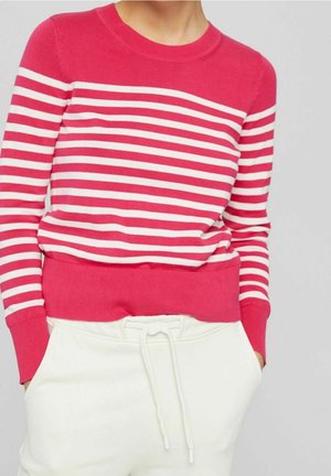 Vrouw in een rood-wit gestreepte trui met ribbels aan de mouwen en onderrand, gecombineerd met witte trekkoordbroek.