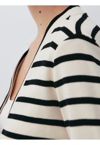 Sweter w paski z kremowym tłem oraz wyraźnymi czarnymi poziomymi paskami, z zamkiem błyskawicznym oraz miękką, lekką teksturą.