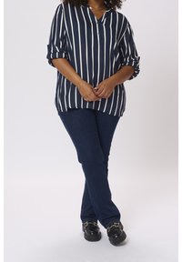 Blouse à rayures marine avec patte de boutonnage, manches retroussées ; associée à un jean denim foncé et des chaussures compensées noires avec des accents dorés.