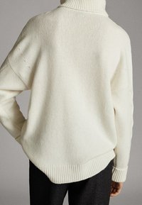 Przesadnie duży, biały sweter z dzianiny z wysokim golfem, ściągaczami przy mankietach i u dołu. Charakteryzuje się teksturowanym wykończeniem i luźnym krojem.