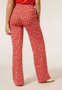 Rode wijde broek met een wit dierenprintpatroon, heeft een hoge taille en een gladde stoftextuur. Minimalistisch ontwerp zonder zichtbare hardware.