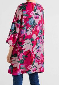 Kwiatowa tunika w jasnoróżowym kolorze z dużymi niebieskimi i białymi kwiatami. Charakteryzuje się luźnym krojem, rękawami o długości trzy czwarte oraz okrągłym dekoltem.